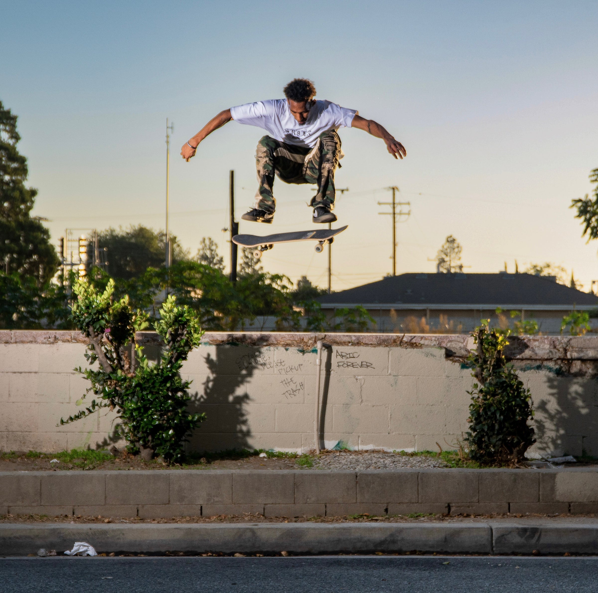 Person skateboarding in mid-air over a concrete wall with trees and power lines in the background.