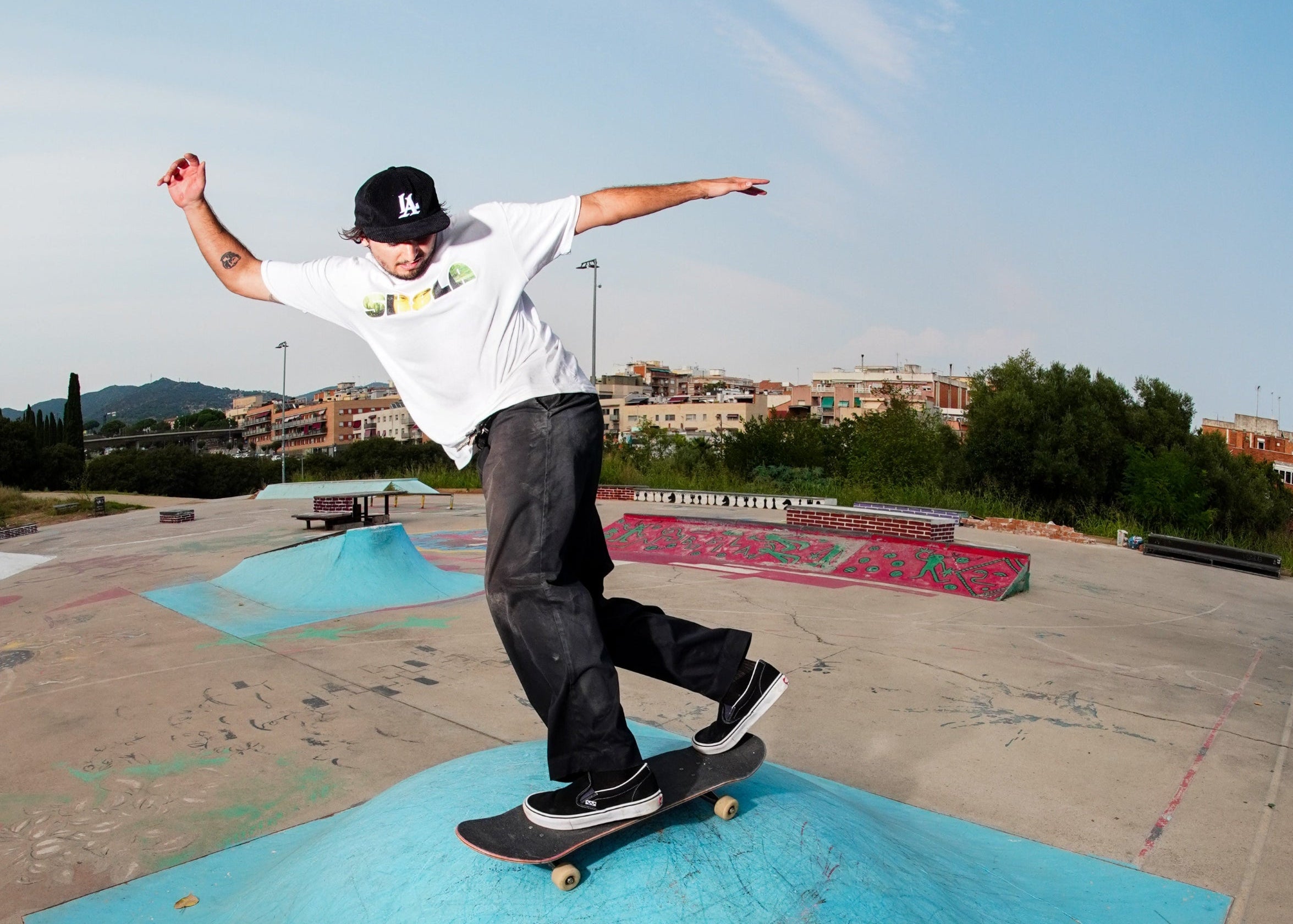 Skateboarder performing a trick on a blue ramp at a skate park with buildings and trees in the background.